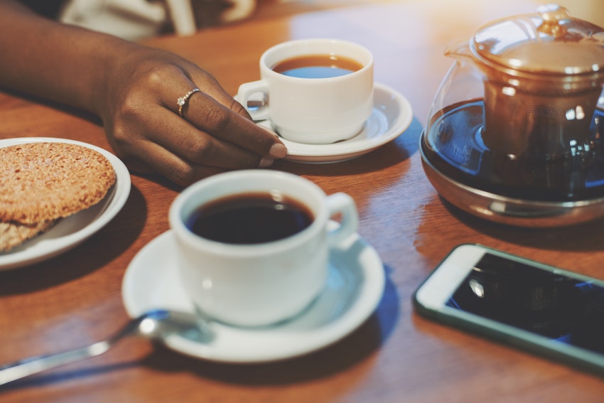 Two mugs of coffee next to a pot of coffee and biscuits