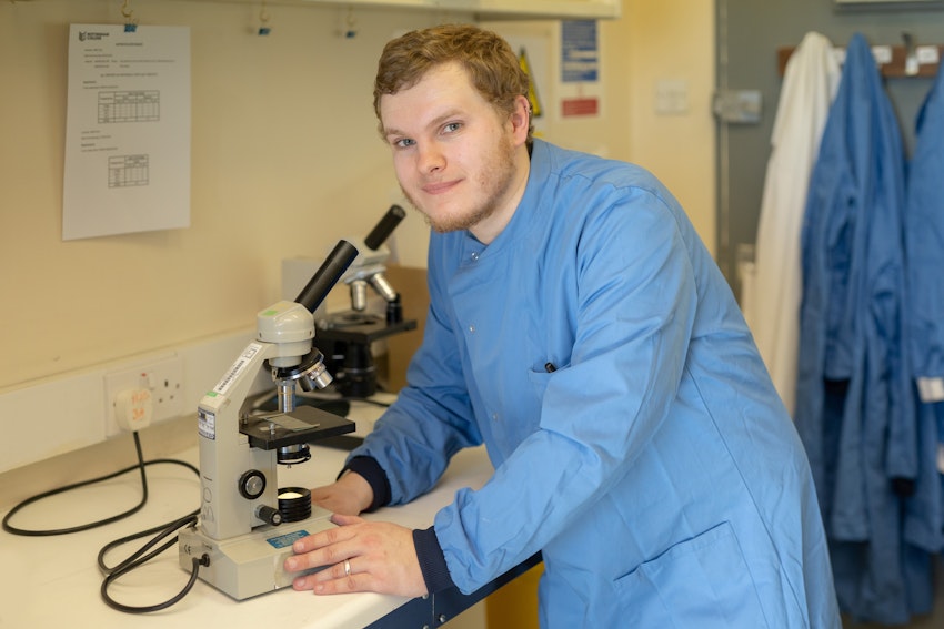 Student smiling whilst holding a microscope