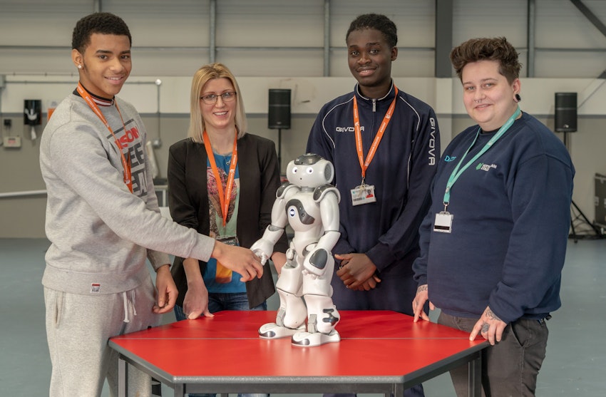 Group of students smiling stood around a robot, with one holding its hand